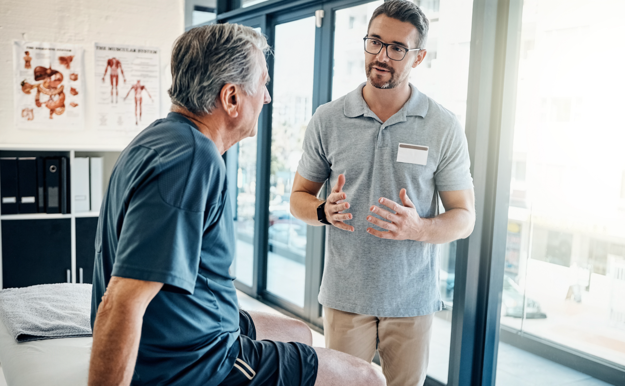 A male medical practitioner explaining a personalized wellness treatment plan to a senior patient sitting on an examination table in a bright Safety Harbor clinical office.
